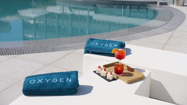 A poolside area with lounge chairs, a towel with "OXYGEN" text, and a tray with a drink and snacks. - Oxygen Lifestyle Hotel  (Rimini)