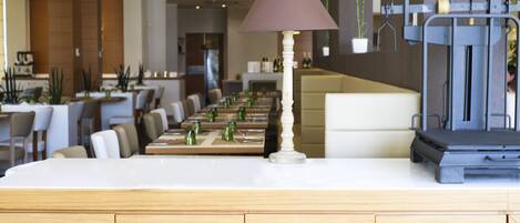 A restaurant with a long counter, tables, chairs, and a lamp.