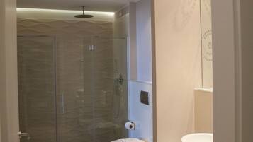 A modern bathroom with a glass-enclosed shower, a toilet, and a sink with a mirror above.