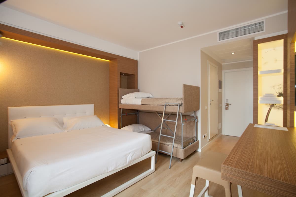 A hotel room with a bunk bed, a single bed, a desk, and a chair.