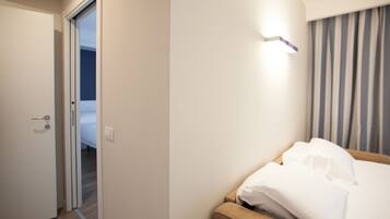 A hotel room with a bed, a door, and a light fixture on the wall.