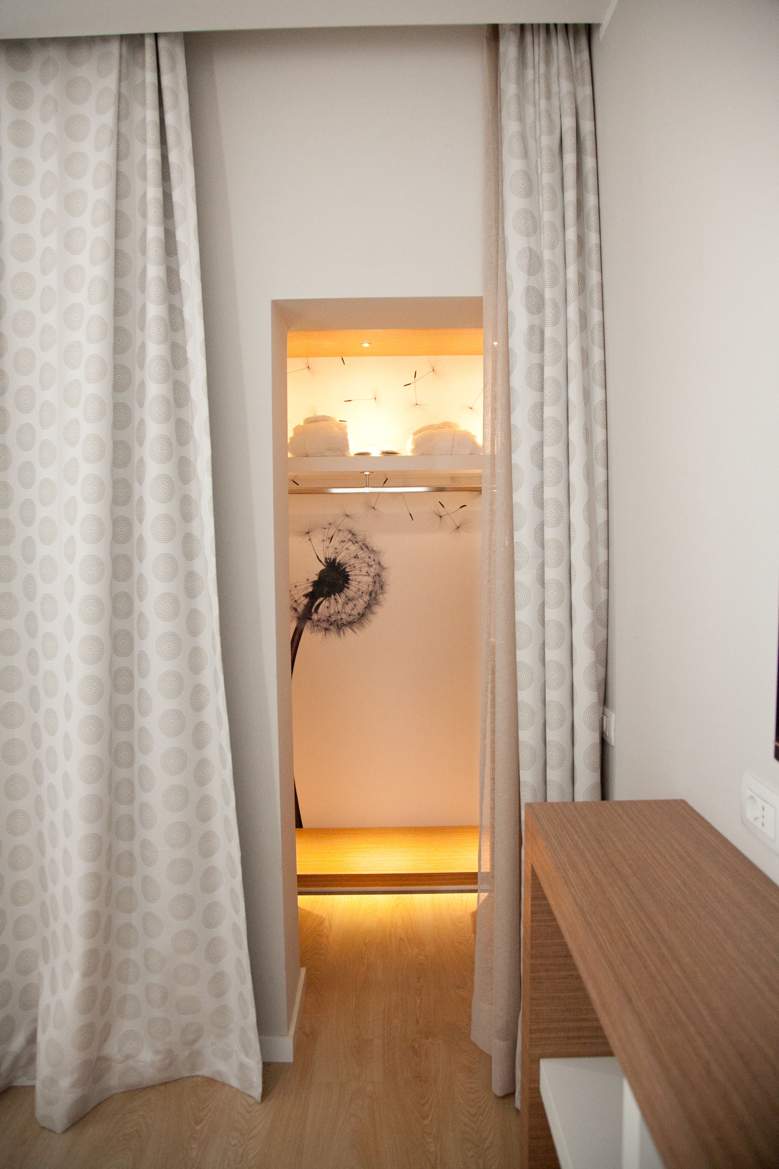 Une pièce avec un bureau en bois, un rideau blanc orné d’un motif circulaire et une décoration représentant un pissenlit sur le mur.