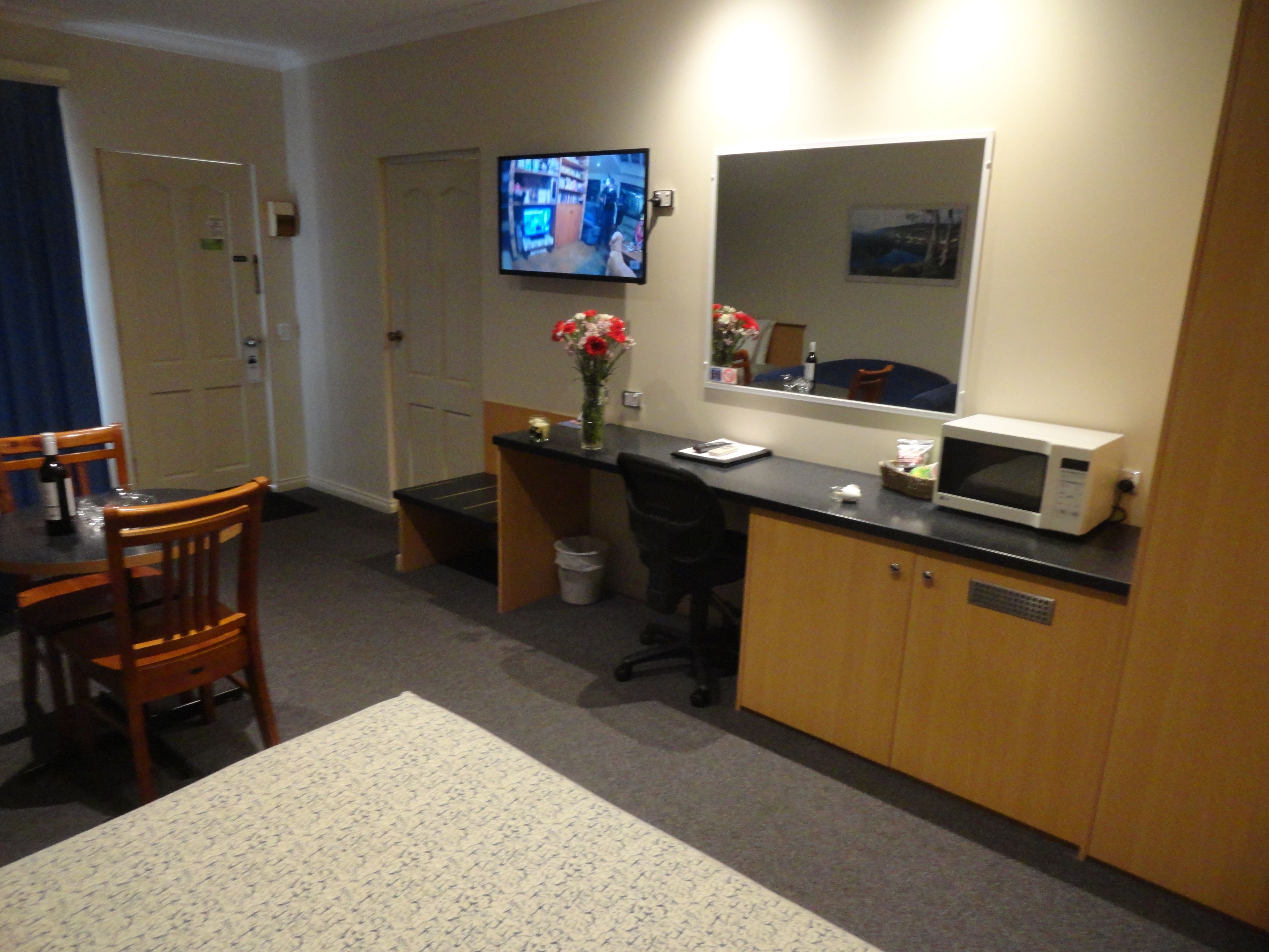 Habitación de hotel con comedor, escritorio con ordenador, microondas y televisor en la pared.