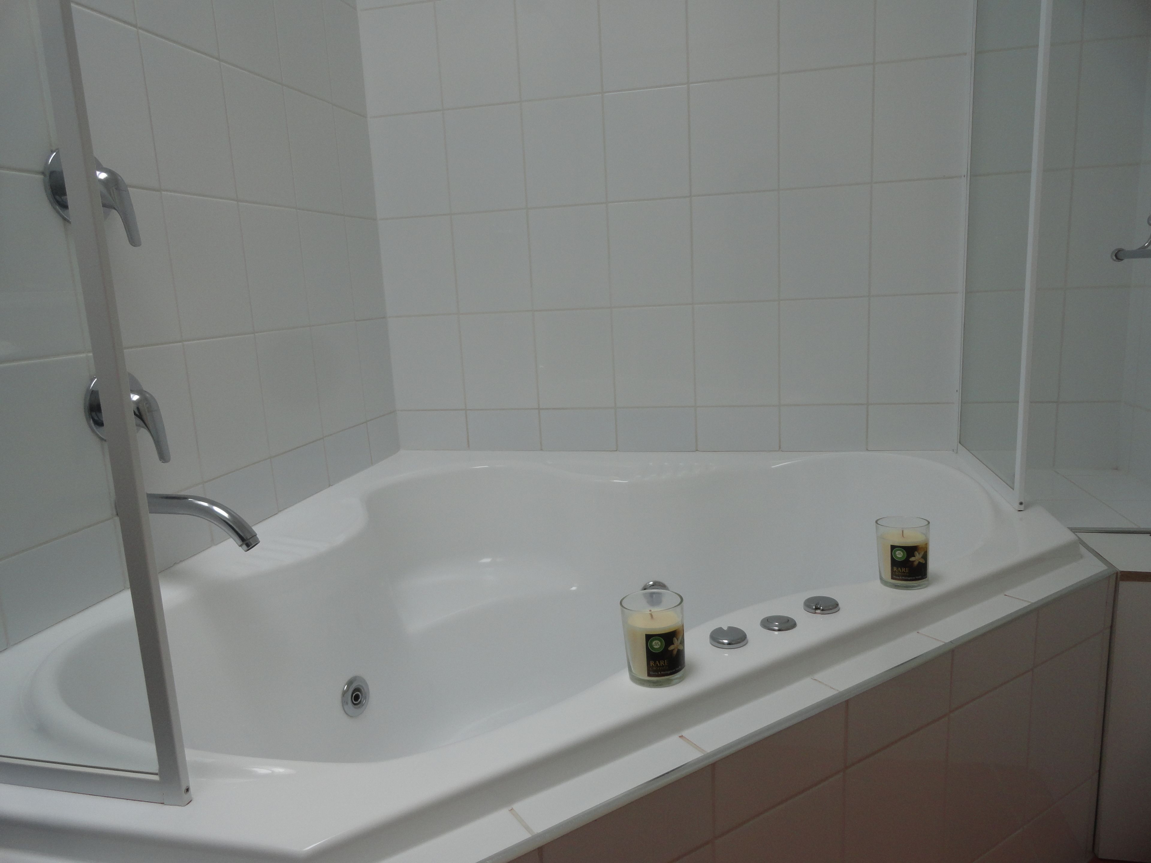 Una bañera blanca con dos velas y un vaso en el borde.