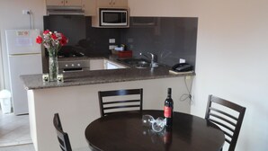 A small kitchen with a microwave, sink, and cabinets. There is a dining table with chairs and a vase with flowers. - Victoria Lodge Motor Inn And Apartments (Portland)