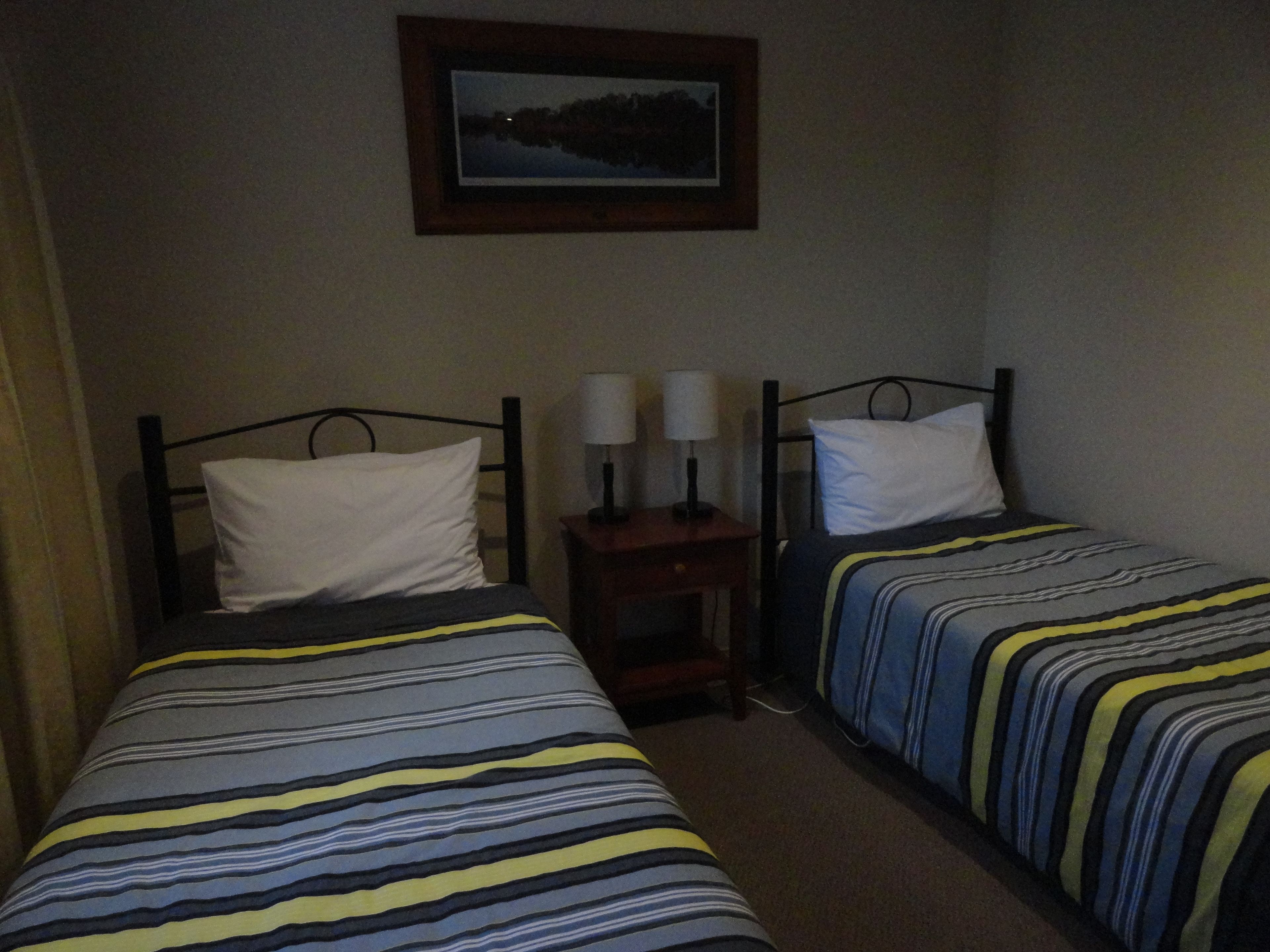 Una habitación con dos camas individuales, cada una con una colcha a rayas y almohadas blancas. Encima de las camas, hay un cuadro enmarcado en la pared.