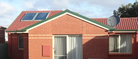 Una casa de ladrillo con techo rojo, una antena parabólica y una ventana con cortinas.