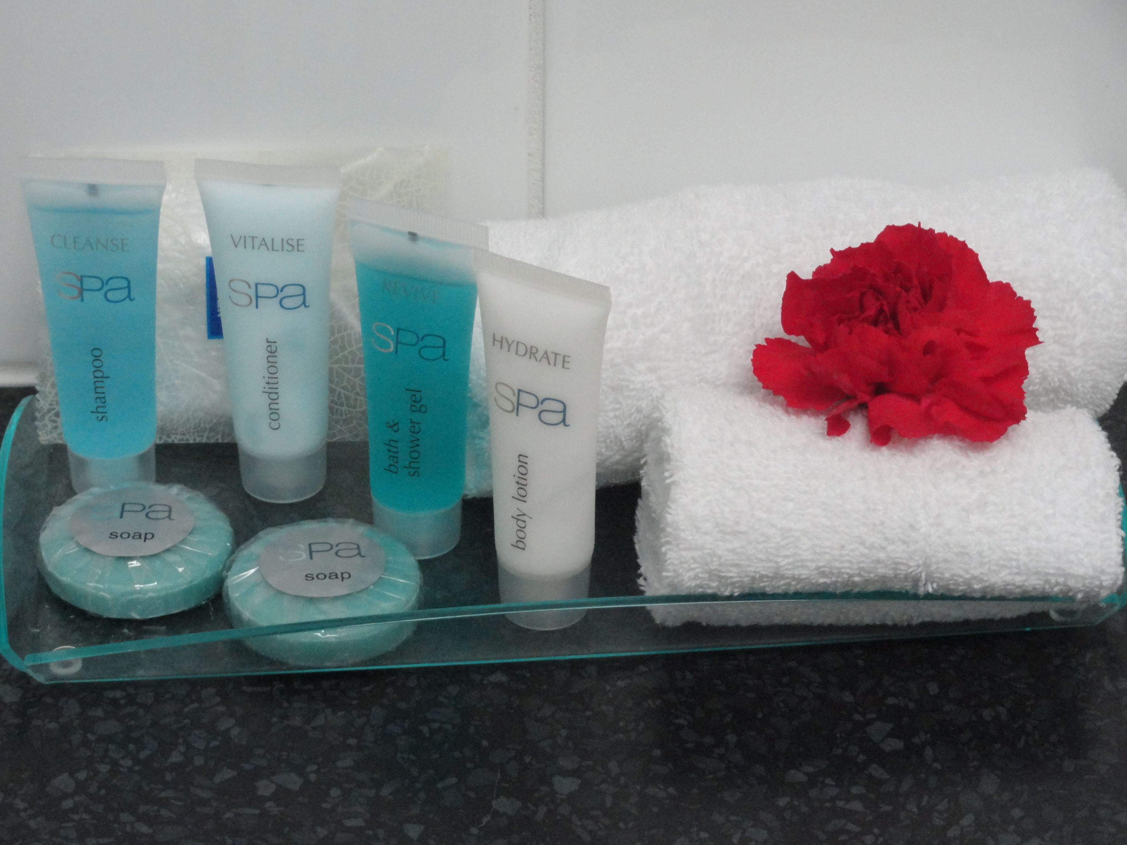 Een glazen dienblad met verzorgingsproducten voor de spa, zoals shampoo, conditioner, bodylotion en zeep.