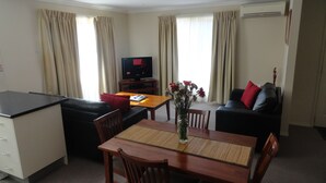 A hotel room with a dining area, a TV, a sofa, and a small table with a vase of flowers. - Victoria Lodge Motor Inn And Apartments (Portland)