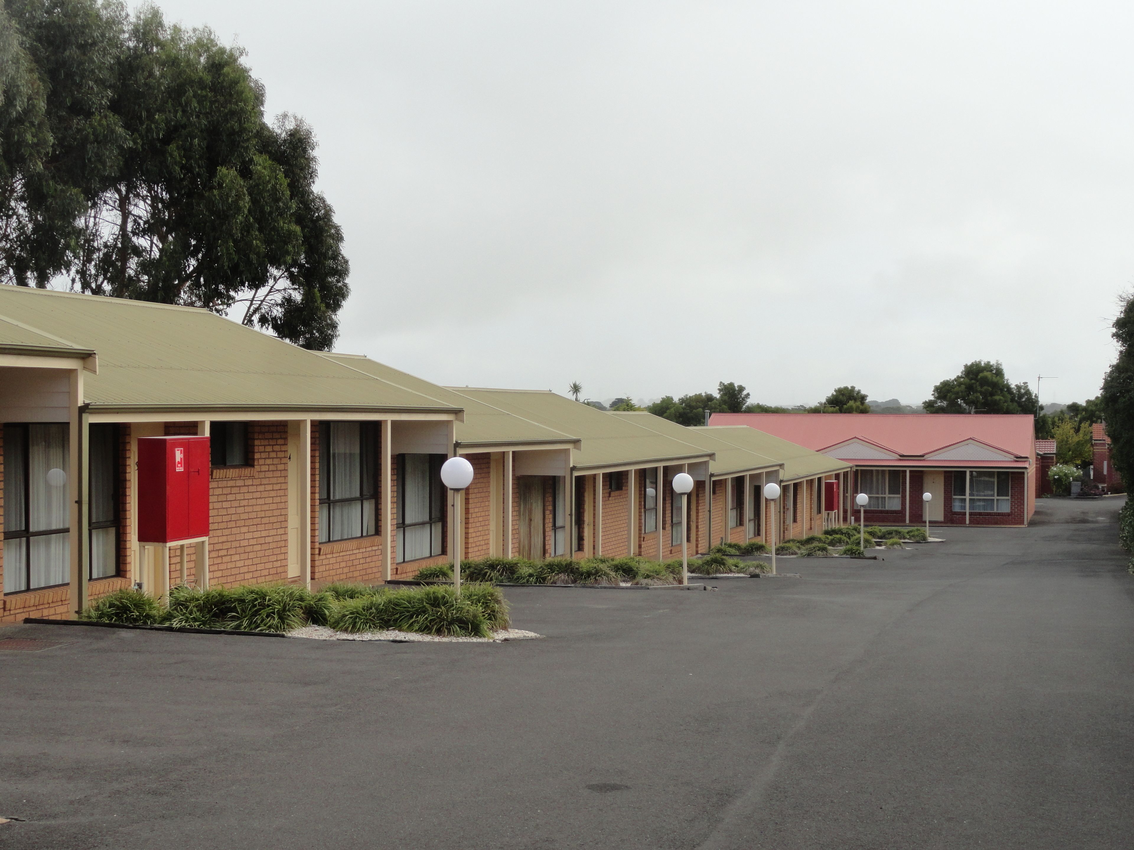 A row of motel buildings with individual rooms, each featuring a door, windows, and a small garden area.