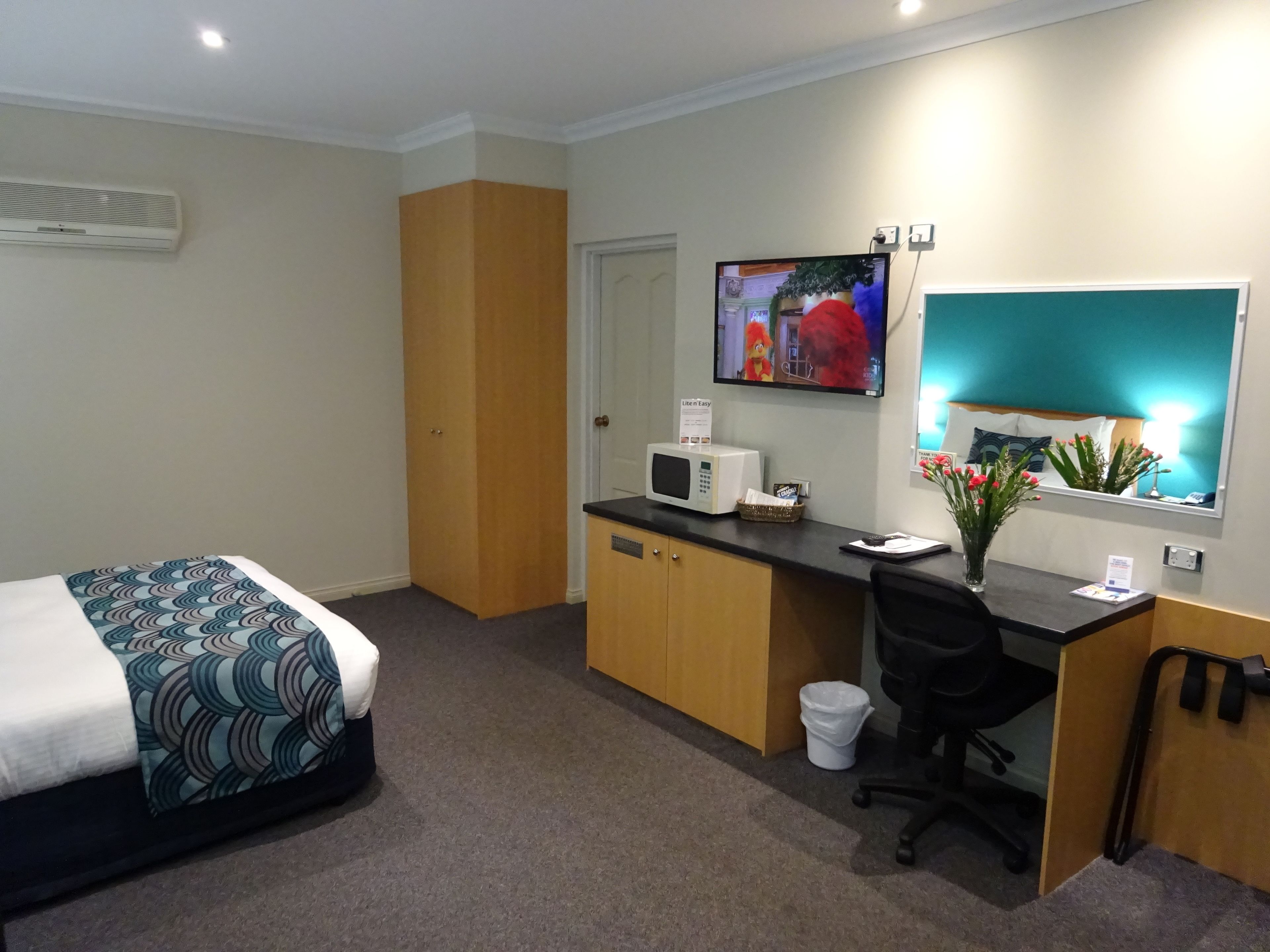 Habitación de hotel con cama, escritorio con computadora, microondas, basurero y ventana con vista al exterior.