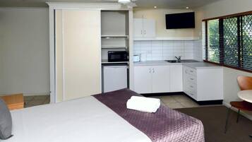 A compact hotel room with a bed, a small kitchenette, a dining area, and a window with blinds.