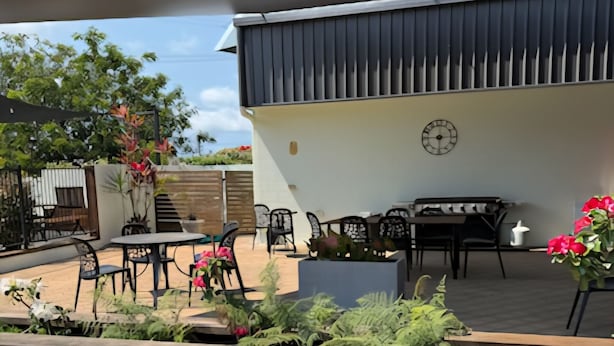 Área de pátio ao ar livre com mesa e cadeiras para refeições, rodeada por plantas e um banco de madeira.