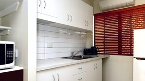Cozinha com armários brancos, micro-ondas, torradeira e janela com persianas.