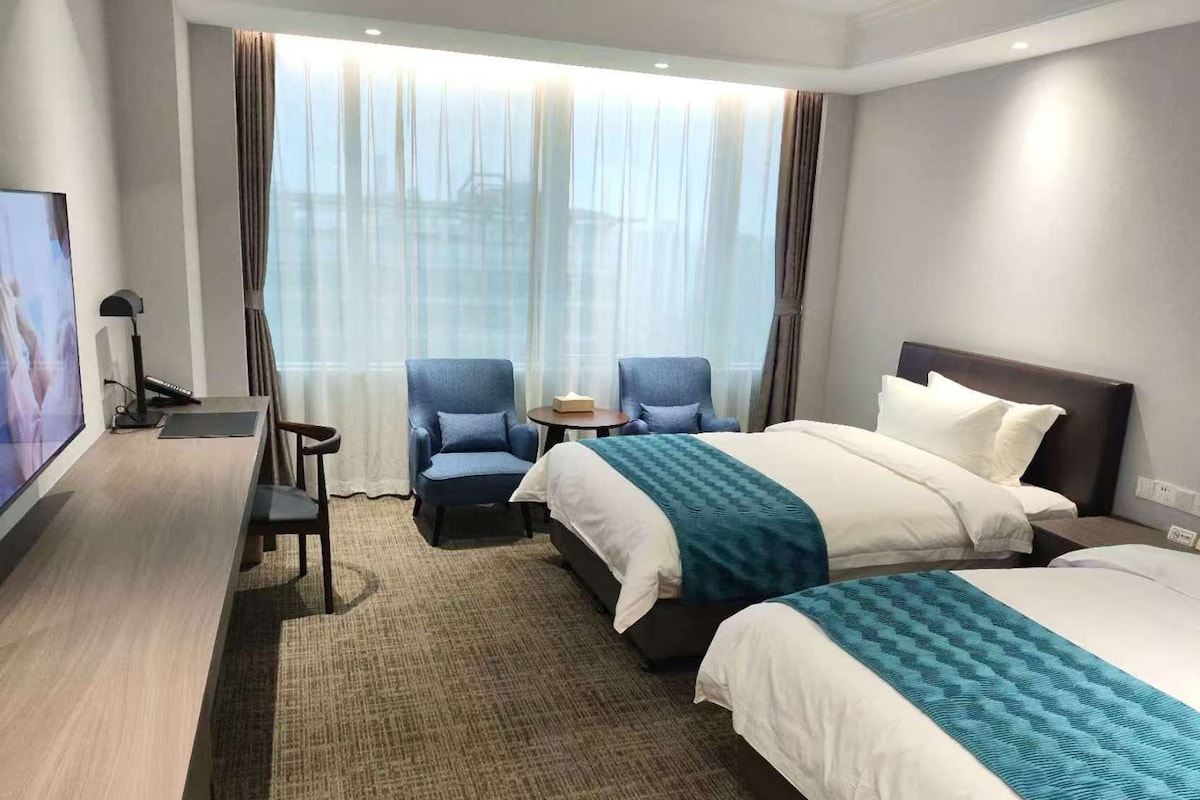 Una habitación de hotel con dos camas, un escritorio, un televisor y una zona de estar con sillones.