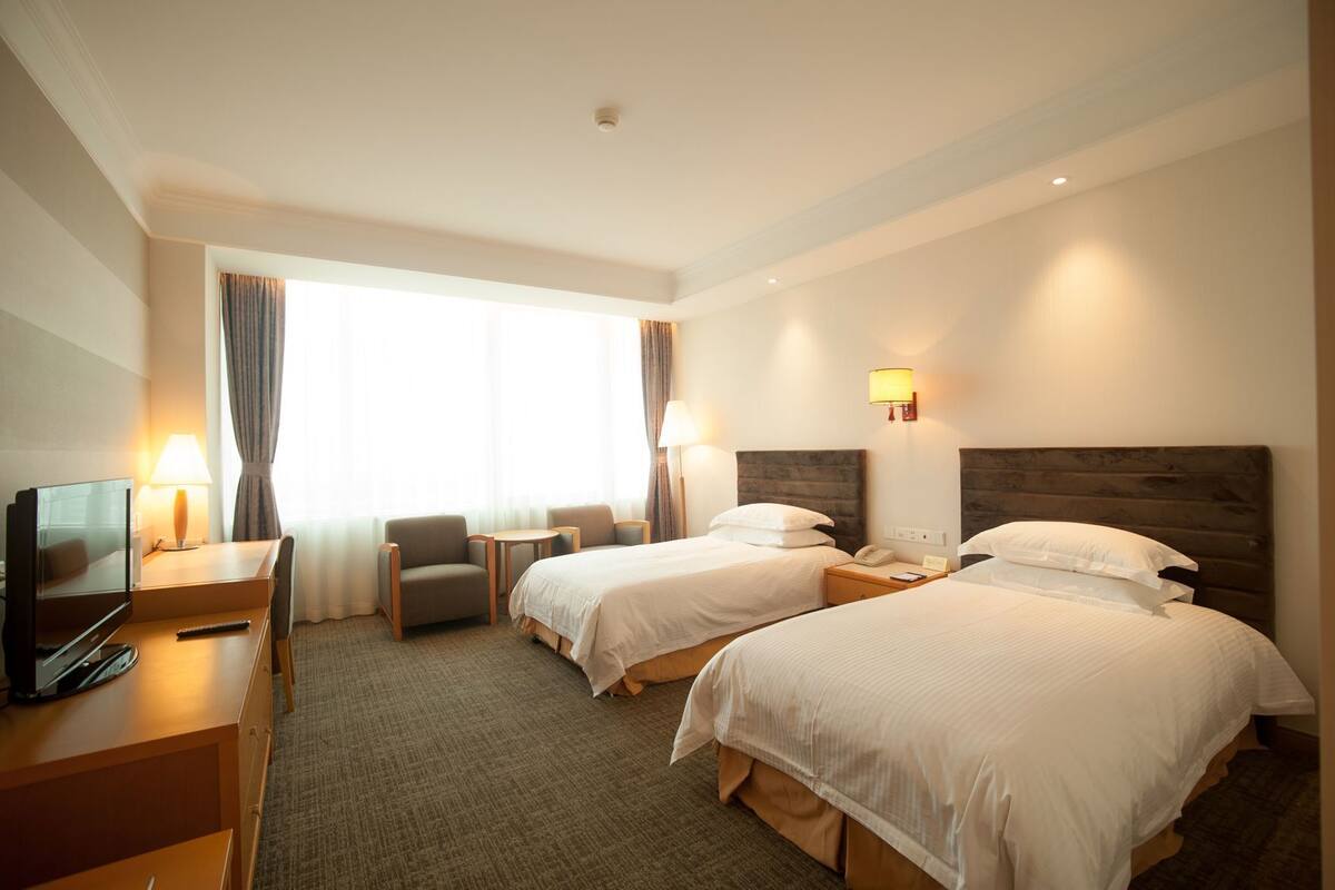 Een hotelkamer met twee bedden, een bureau met een televisie, een stoel en een lamp.