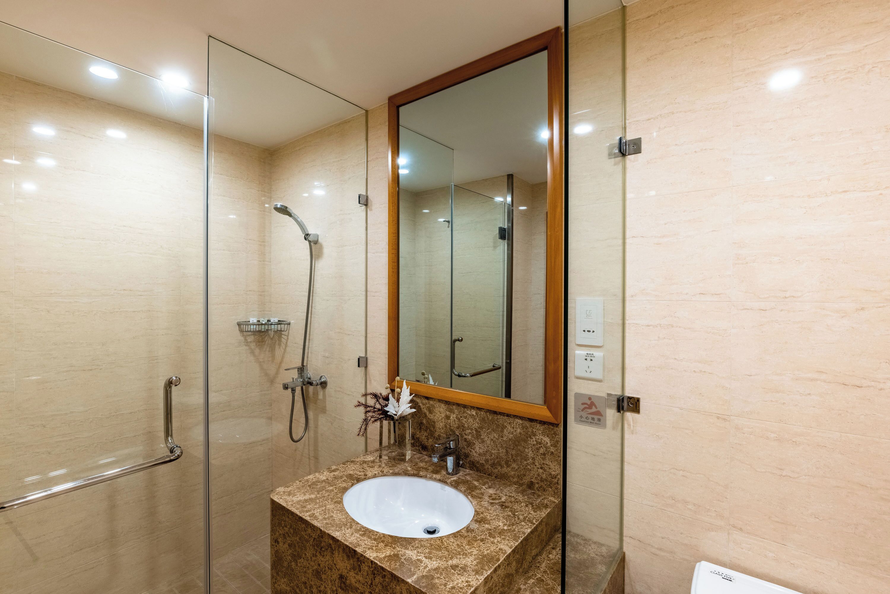 A modern bathroom with a glass shower enclosure, a marble sink, and a large mirror.