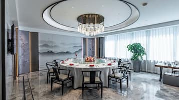 A modern dining room with a round table, chairs, a chandelier, and a large potted plant.