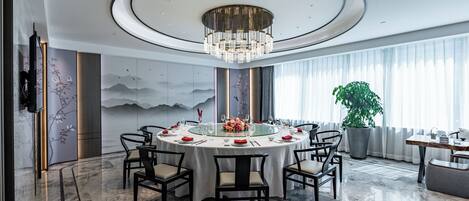 Une salle à manger moderne avec une table ronde, des chaises, un lustre et une grande plante en pot.