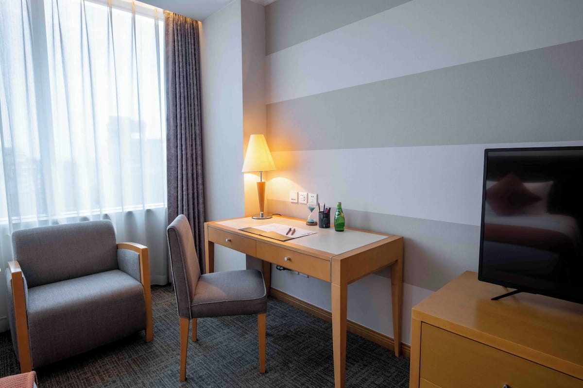 Een hotelkamer met een bureau, stoel, televisie, lamp en een raam met gordijnen.