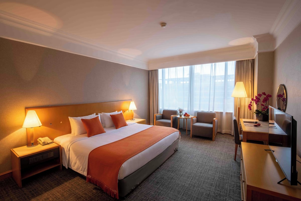 Een hotelkamer met een groot bed, twee nachtkastjes met lampen, een bureau met een computer, een stoel en een tafeltje met een bloemenvaas.