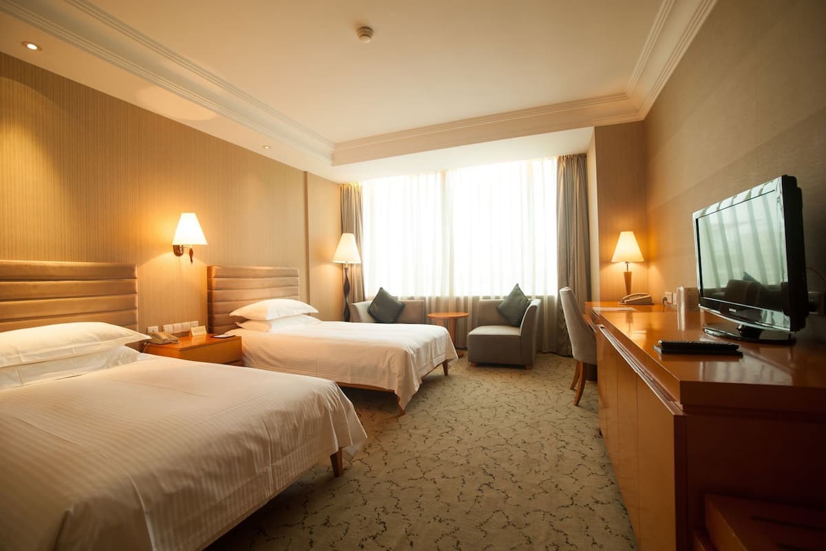 Een hotelkamer met twee bedden, een bureau met een televisie en een stoel.