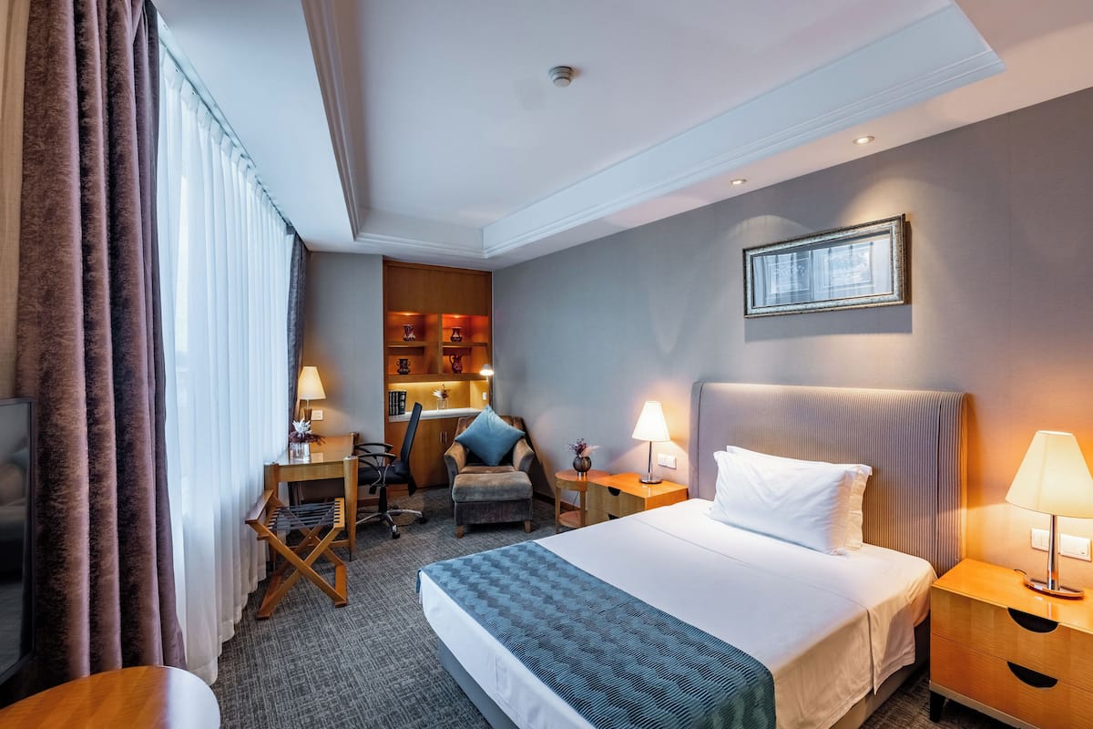 Een hotelkamer met een bed, een bureau, een stoel, een kleine kitchenette en een raam met jaloezieën.