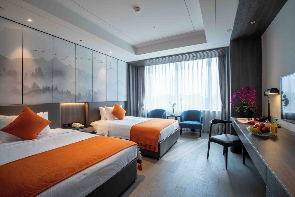 Een hotelkamer met twee bedden, een bureau, een stoel en een groot raam met gordijnen.