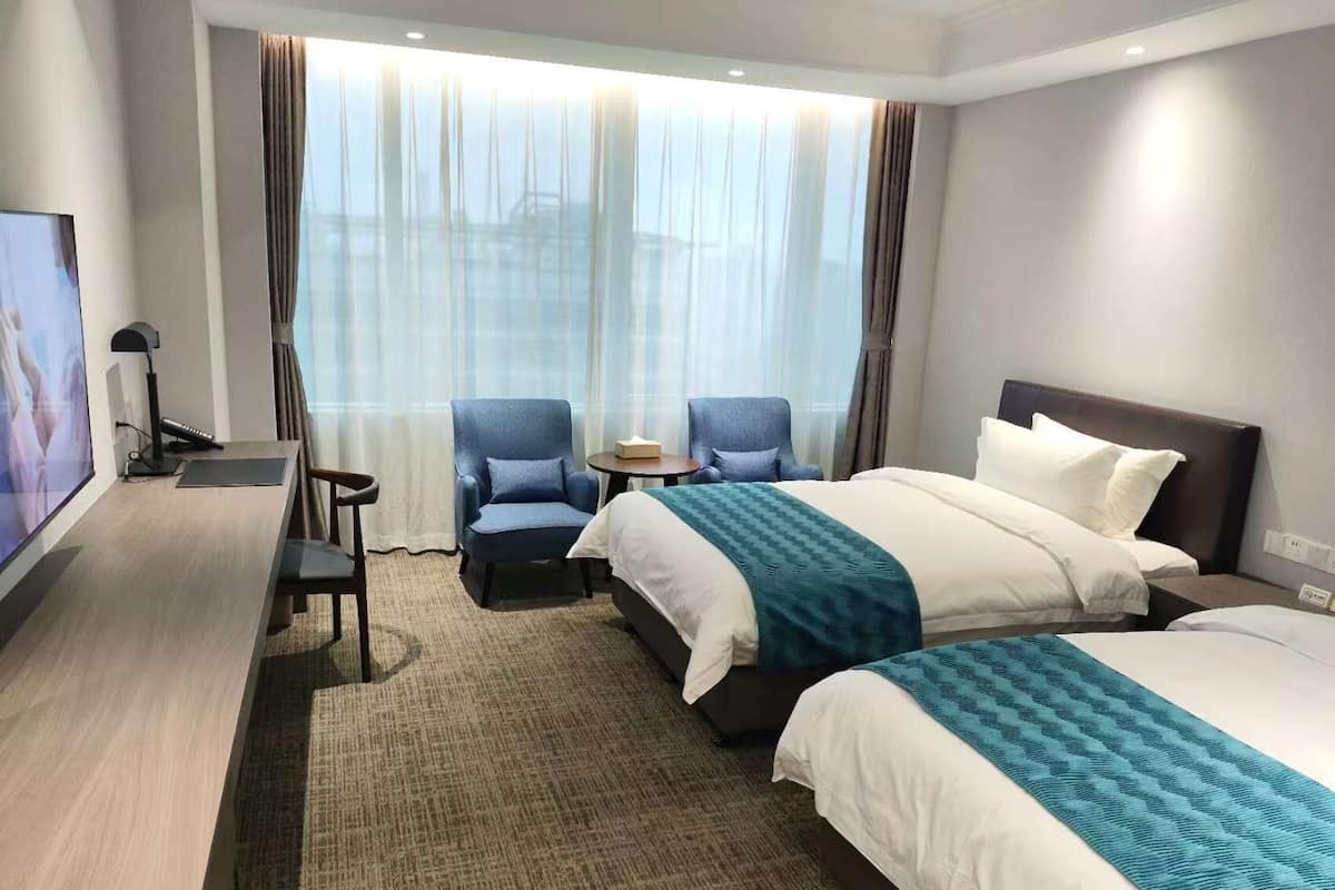 Een hotelkamer met een bed, twee fauteuils, een bureau met een computer en een televisie.