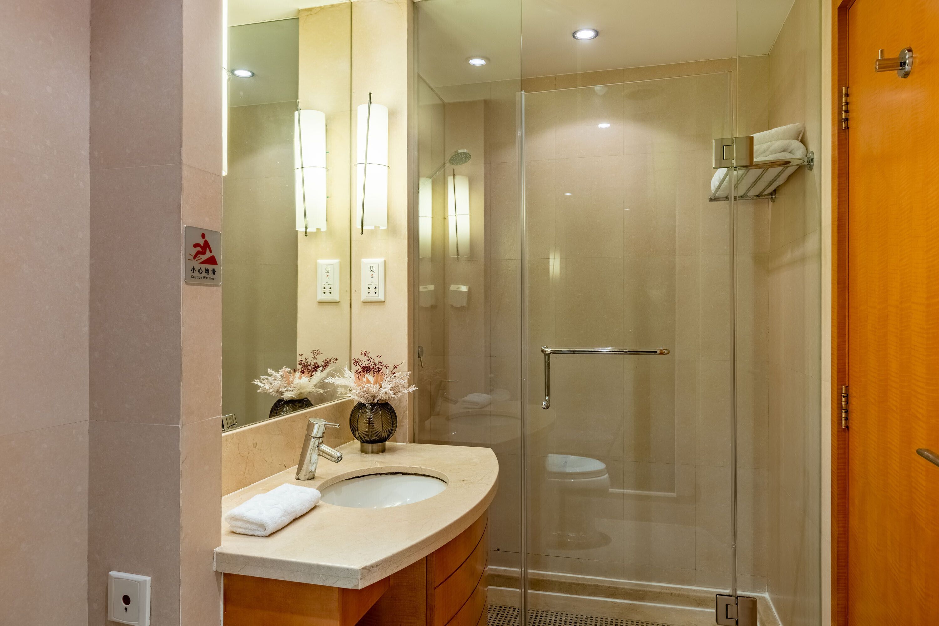 A modern bathroom with a glass-enclosed shower, a sink with a towel, and a mirror.