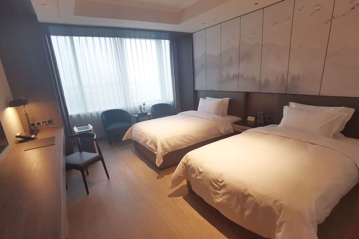 Een hotelkamer met twee bedden, een bureau, een stoel en uitzicht op bergen door het raam.
