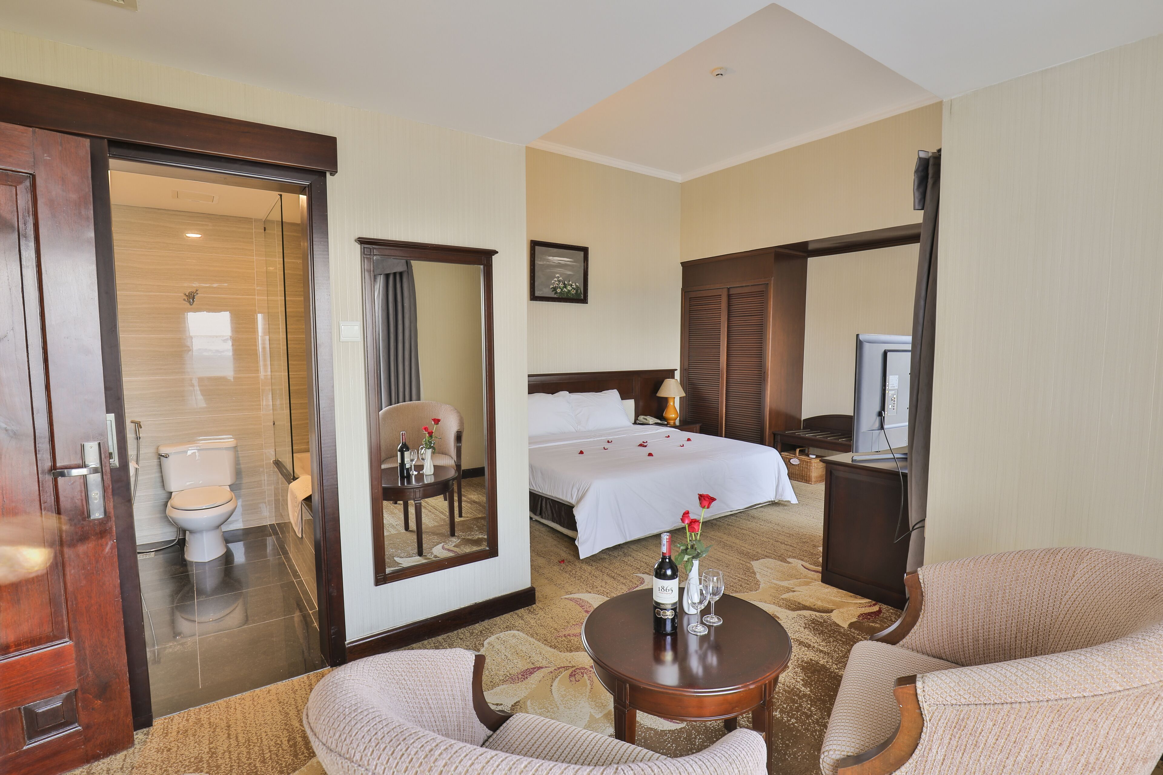 Quarto de hotel com cama, escrivaninha, cadeira, televisão e banheiro.