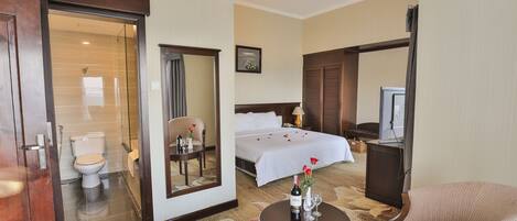 Quarto de hotel com cama, escrivaninha, cadeira, televisão e banheiro.