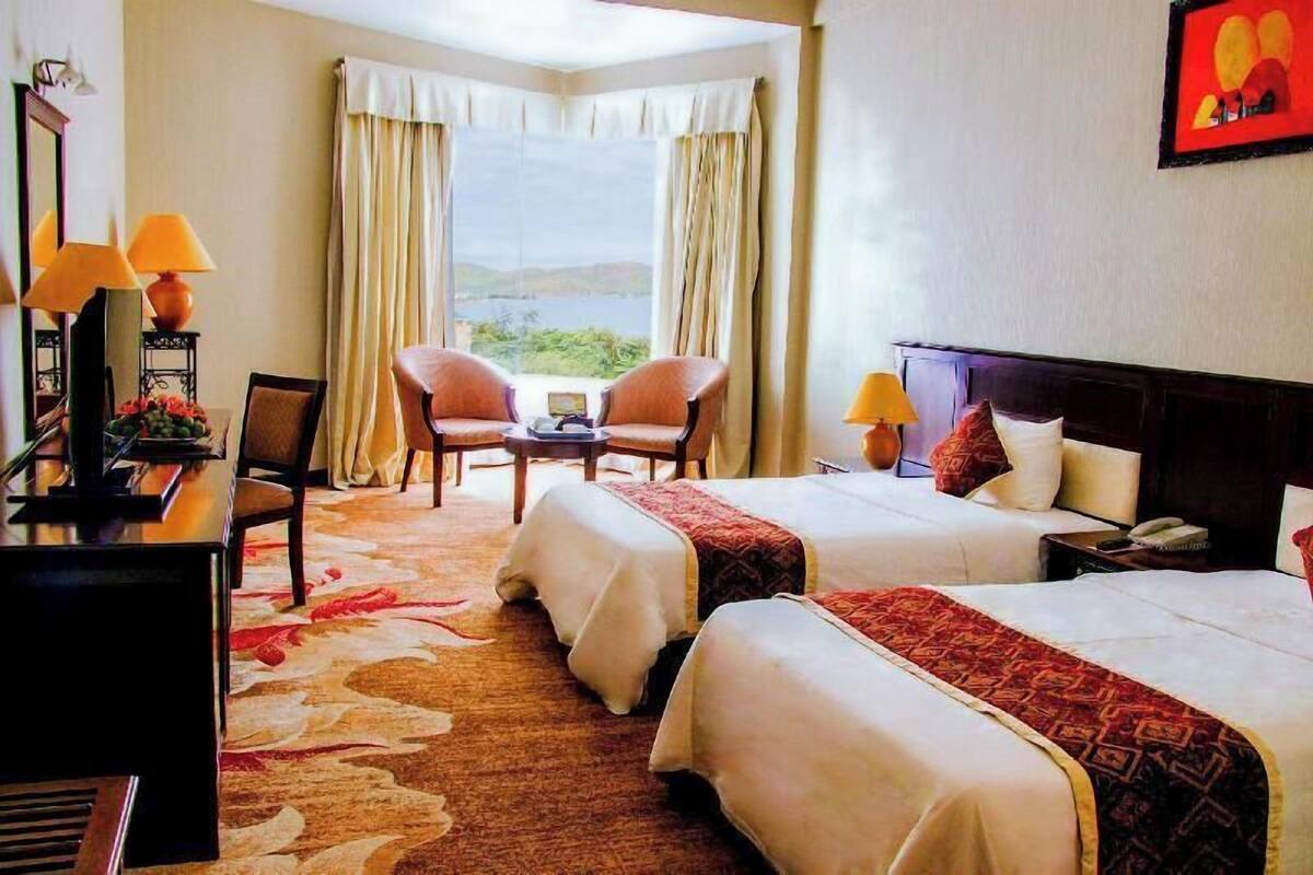 Une chambre d’hôtel avec deux lits, un bureau avec une lampe, une chaise et une vue sur l’extérieur.