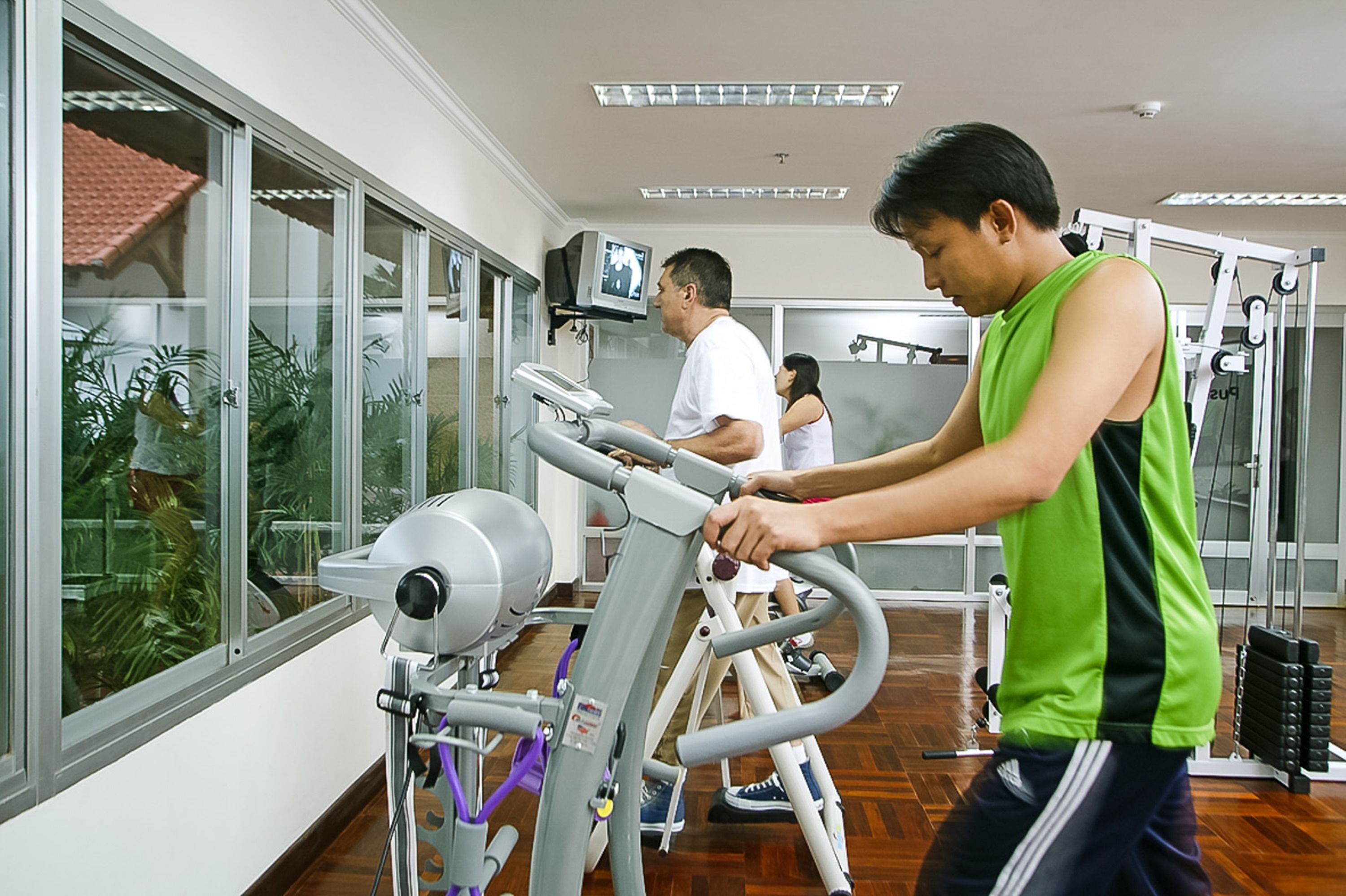 A gym with exercise equipment, large windows, and a view of palm trees.