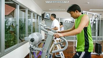 A gym with exercise equipment, large windows, and a view of palm trees.