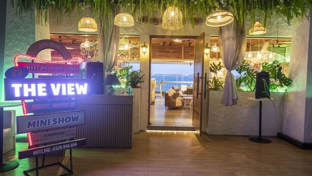 Zona de recepción con un cartel anunciando los eventos 'The View' y 'Mini Show', suelo de madera y plantas colgantes.
