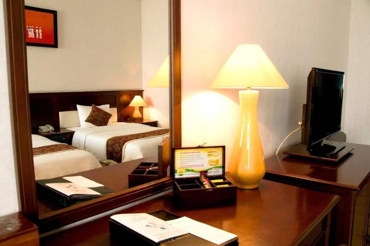 Une chambre d’hôtel avec un lit, des tables de chevet, une lampe, une télévision et un miroir.