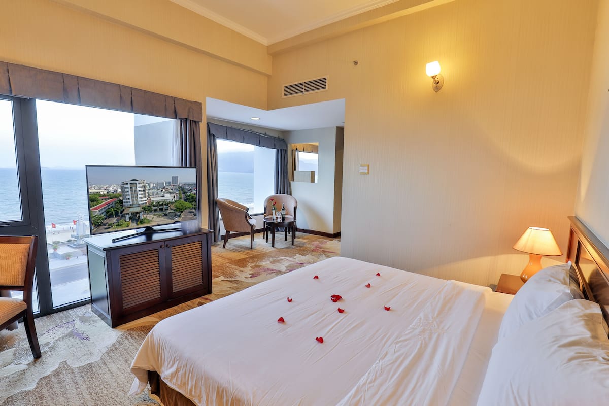 Une chambre d’hôtel avec un lit, un bureau avec une télévision, une chaise et une vue sur la mer.