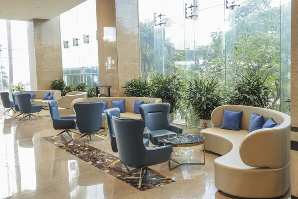 A modern lobby with seating areas, large windows, and indoor plants.