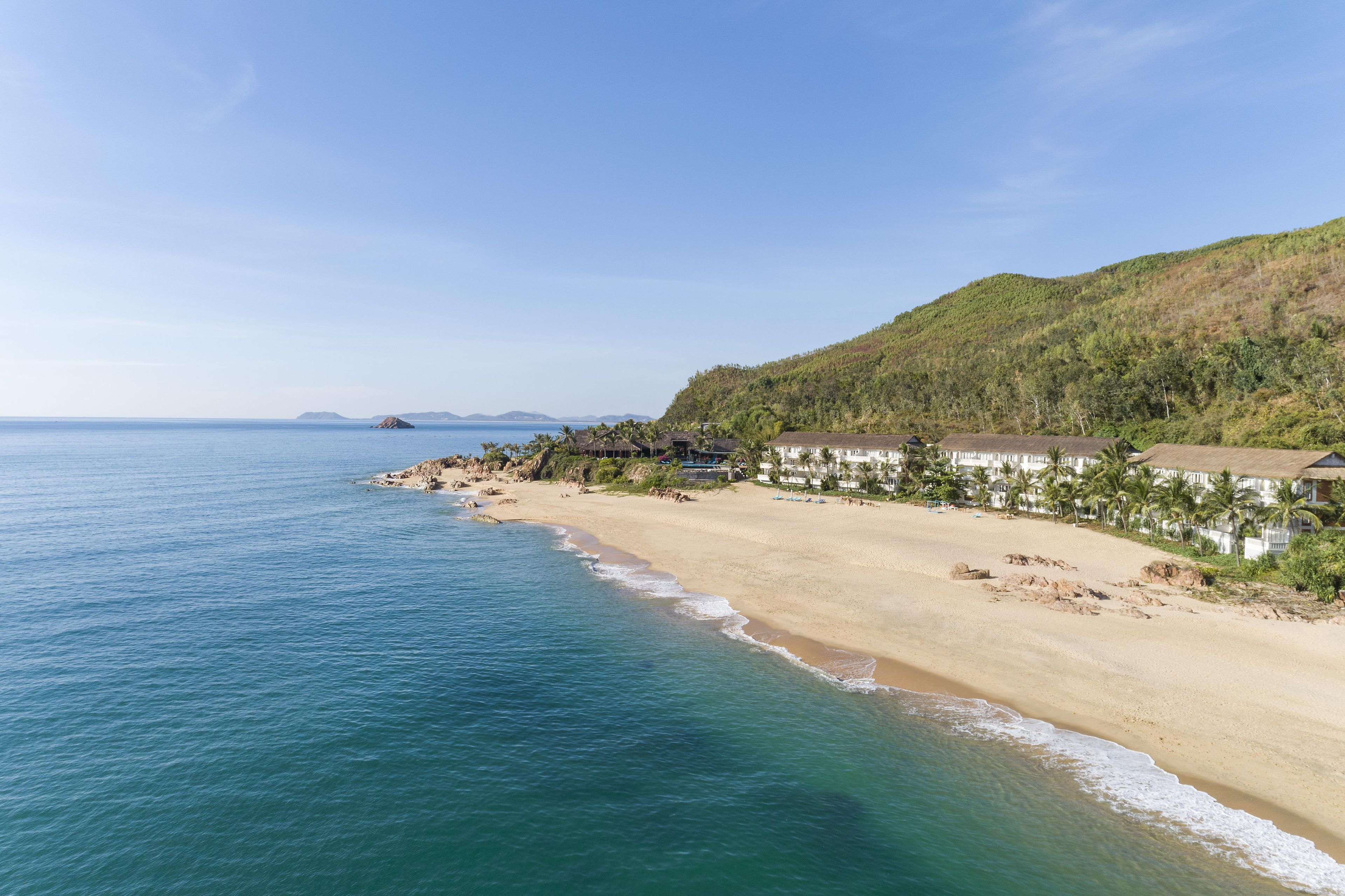 A beach with a clear view of the ocean, a sandy shore, and a hillside with buildings.