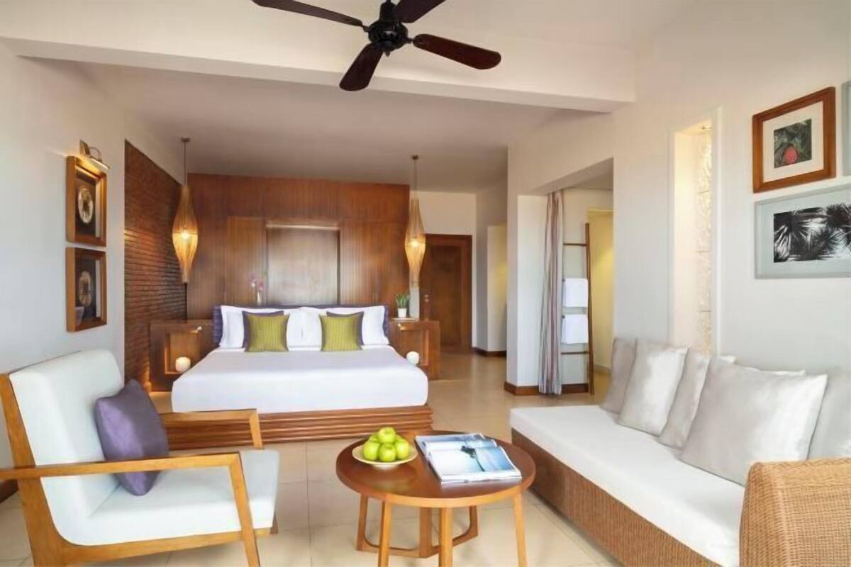A hotel room with a bed, a sofa, a coffee table, and a ceiling fan.