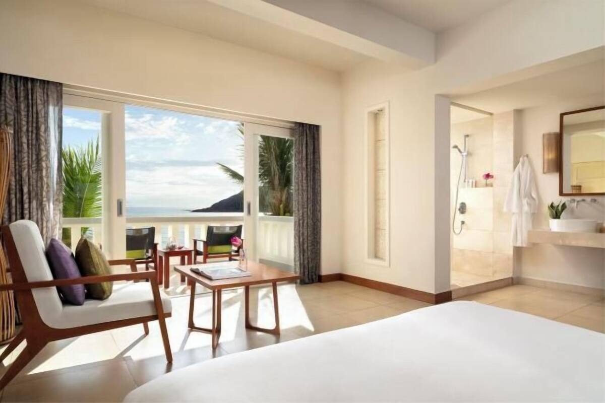 A hotel room with a balcony, a bed, a table, and a bathroom.