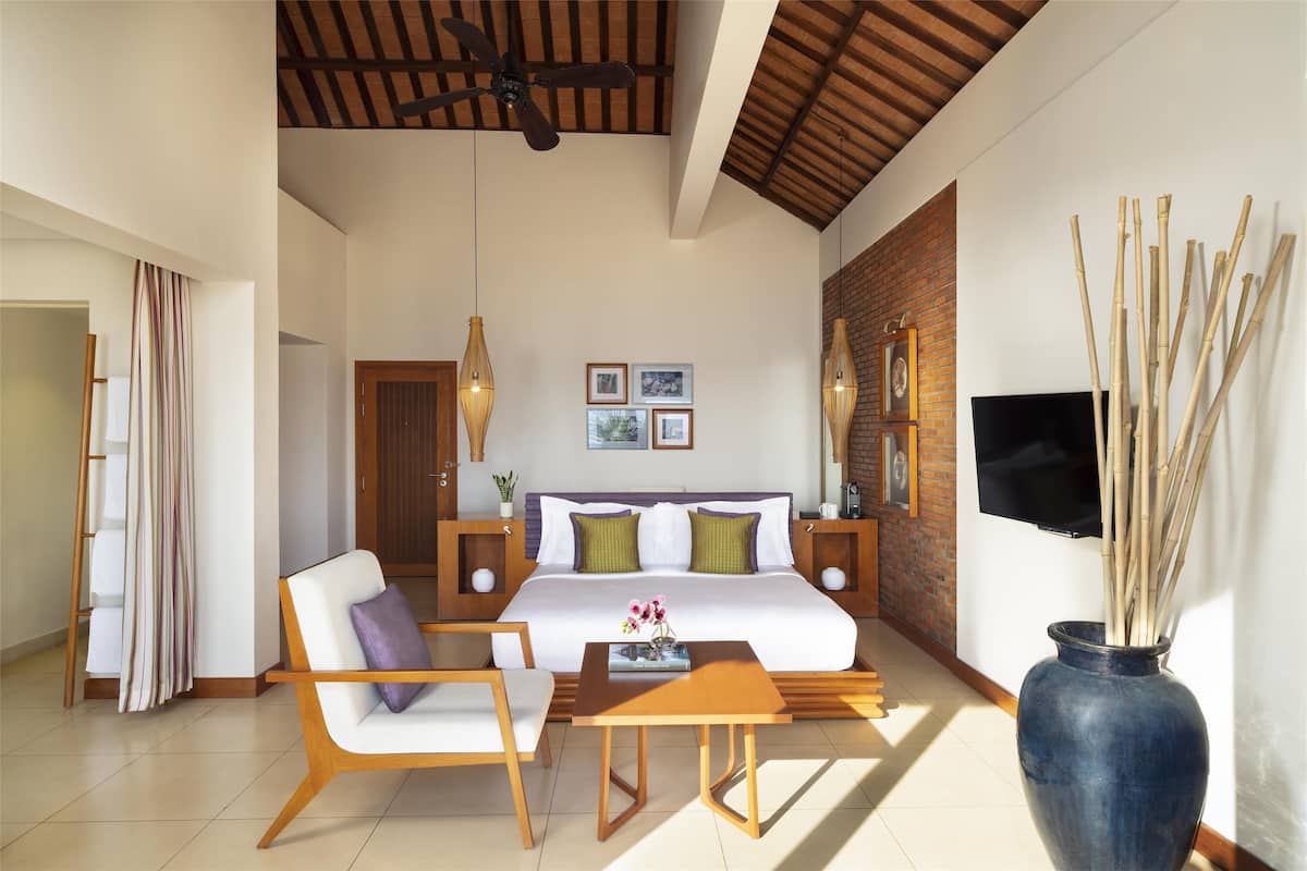 A modern hotel room with a large bed, a TV, a wooden ceiling, and a large vase with sticks.