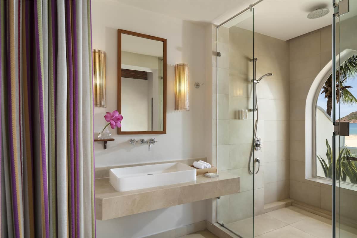 A modern bathroom with a glass-enclosed shower, a large mirror, and a beige countertop.