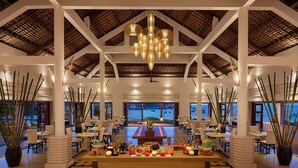 A spacious dining area with a central table, surrounded by chairs, and a view of the sea. - Avani Quy Nhon Resort (Quy Nhon Nam)