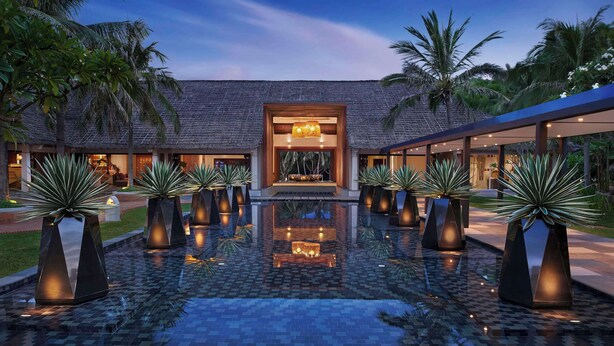 A pool area with a central seating area, surrounded by palm trees and potted plants. - Avani Quy Nhon Resort (Quy Nhon Nam)