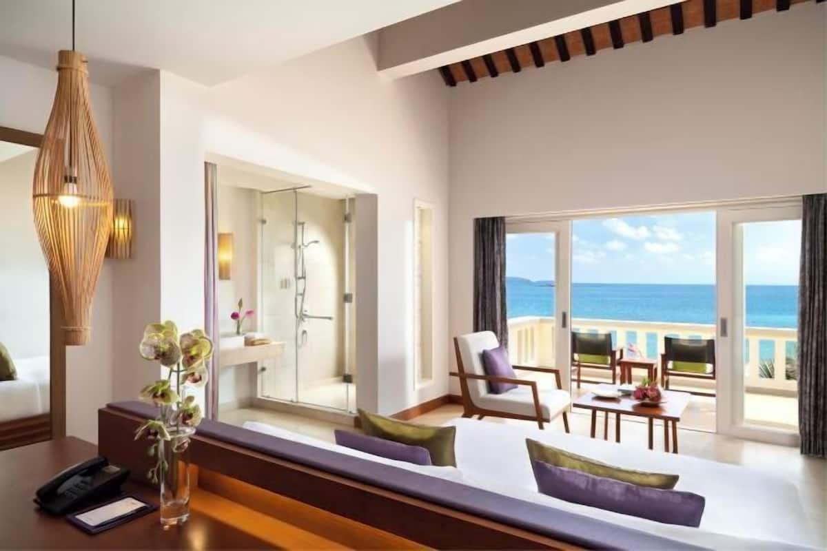 A modern hotel room with a balcony, a sofa, a chair, a table, and a shower area.