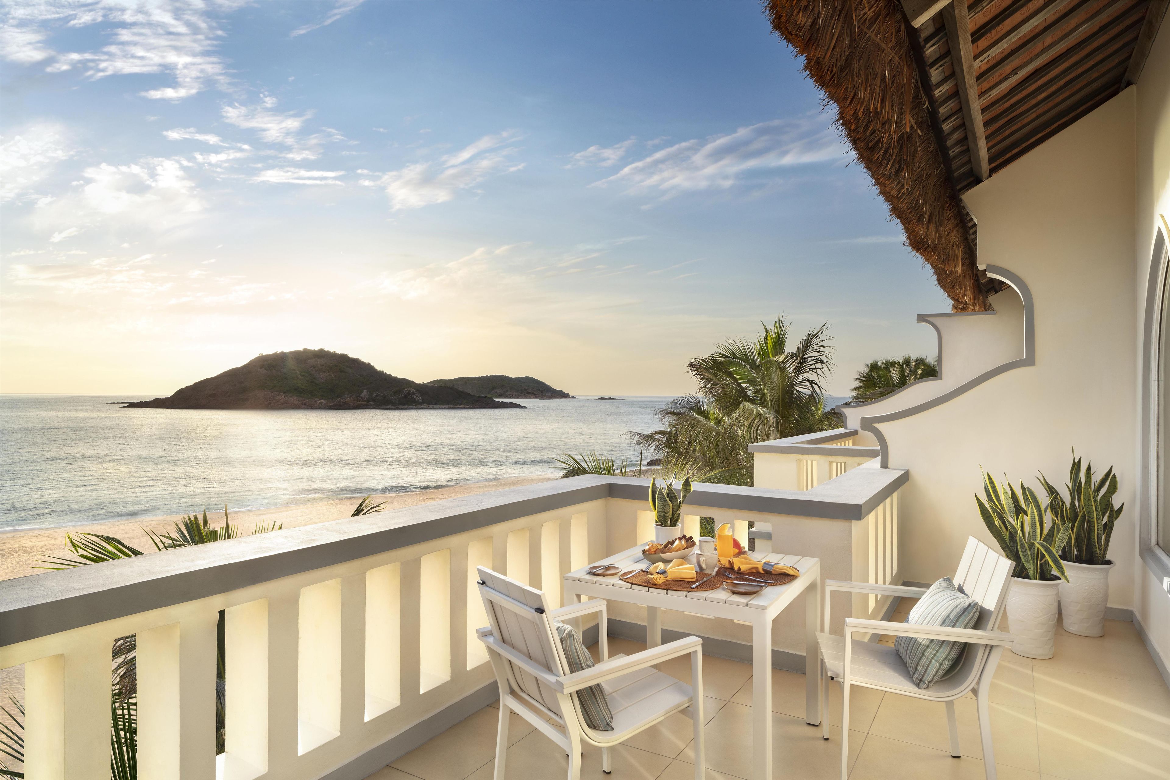 Un balcon avec une table dressée pour deux personnes, donnant sur une plage et la mer.