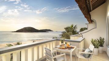 Un balcon avec une table dressée pour deux personnes, donnant sur une plage et la mer.